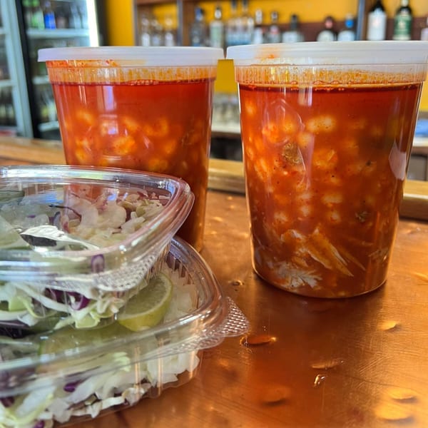 Two large containers of pozole soup and two smaller containers of shredded cabbage and lime.