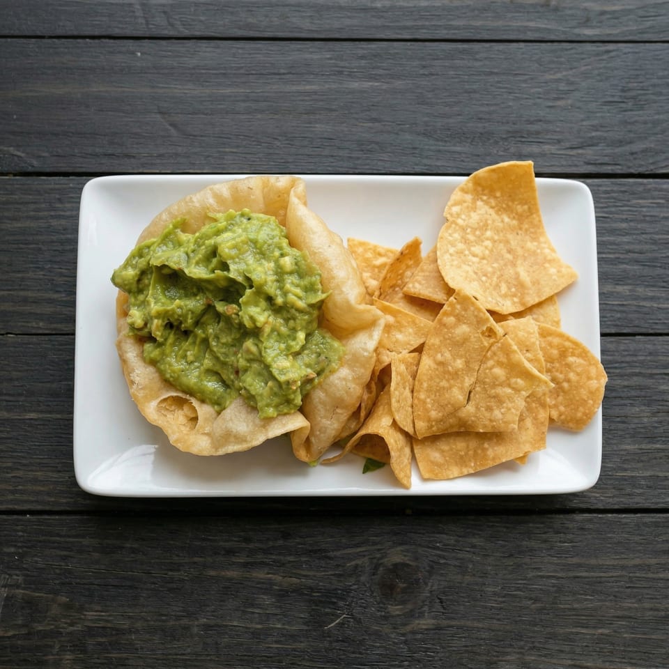 Guacamole in a fried tortilla bowl with tortilla chips on a white rectangular plate.